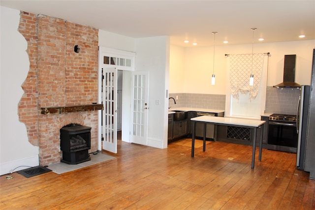 kitchen with tasteful backsplash, decorative light fixtures, wall chimney range hood, stainless steel appliances, and hardwood / wood-style floors