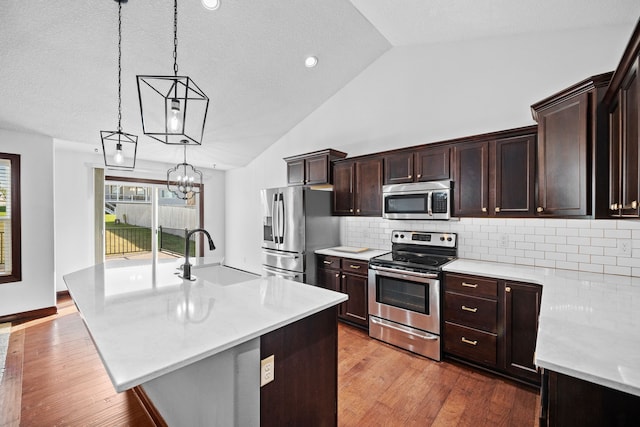 kitchen with decorative light fixtures, a center island with sink, decorative backsplash, sink, and appliances with stainless steel finishes