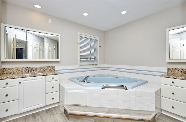 bathroom featuring tiled tub, vanity, and hardwood / wood-style floors