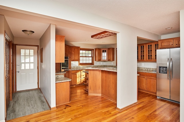 kitchen with light stone counters, light hardwood / wood-style floors, kitchen peninsula, appliances with stainless steel finishes, and a textured ceiling