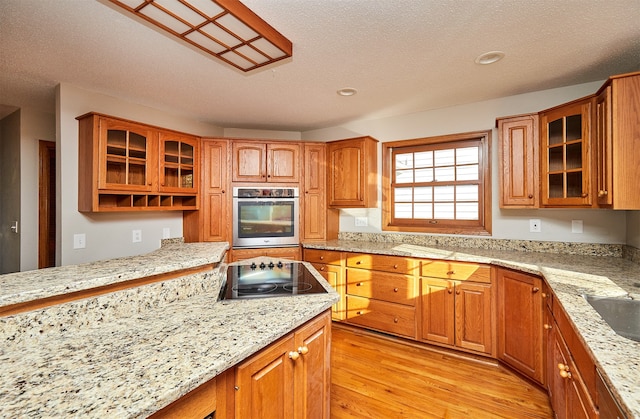 kitchen featuring black electric cooktop, light stone counters, oven, light hardwood / wood-style floors, and a textured ceiling