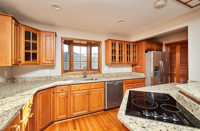 kitchen with a textured ceiling, light hardwood / wood-style floors, stainless steel appliances, and light stone countertops