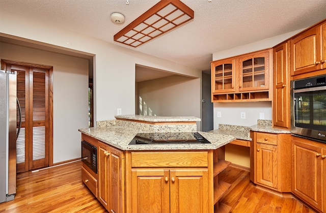 kitchen with kitchen peninsula, black appliances, and light hardwood / wood-style floors