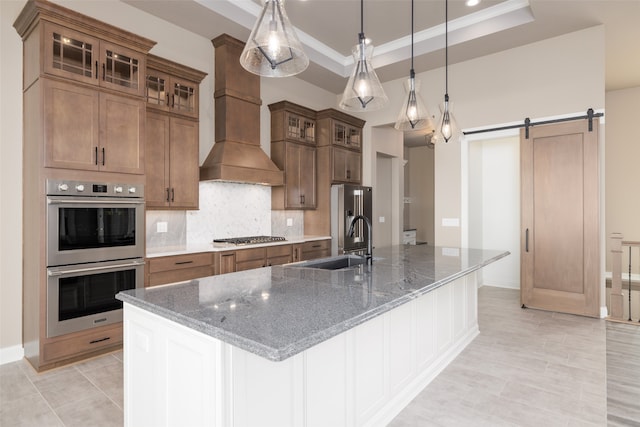 kitchen featuring a large island with sink, a raised ceiling, pendant lighting, a barn door, and appliances with stainless steel finishes