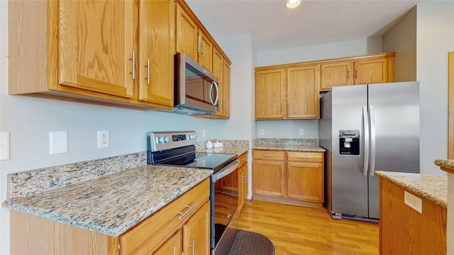 kitchen with appliances with stainless steel finishes, light wood-type flooring, and light stone counters