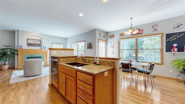 kitchen with hanging light fixtures, sink, a kitchen island with sink, a chandelier, and light wood-type flooring