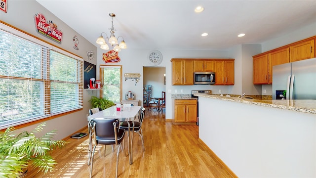 kitchen featuring light wood-type flooring, light stone countertops, pendant lighting, an inviting chandelier, and appliances with stainless steel finishes