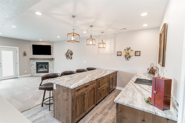 kitchen with light stone countertops, sink, hanging light fixtures, a fireplace, and a kitchen island