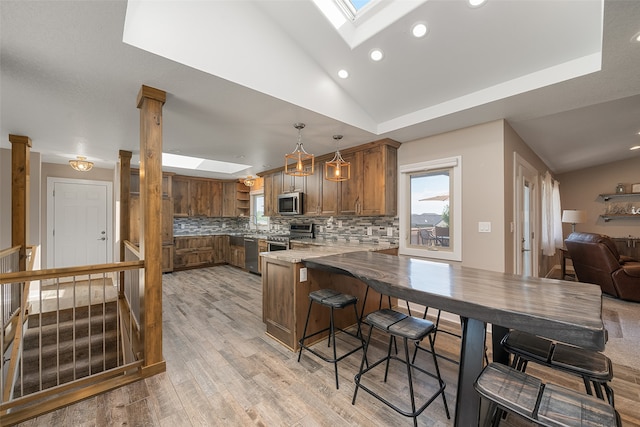 kitchen with lofted ceiling with skylight, decorative backsplash, appliances with stainless steel finishes, a kitchen bar, and kitchen peninsula