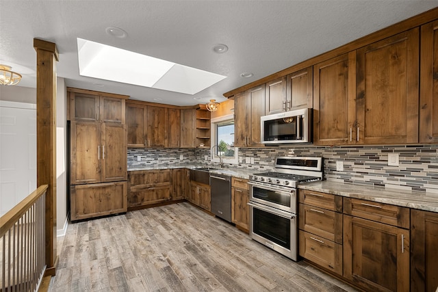 kitchen with sink, a skylight, appliances with stainless steel finishes, light hardwood / wood-style floors, and light stone counters