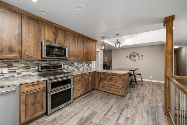 kitchen featuring decorative light fixtures, kitchen peninsula, stainless steel appliances, and tasteful backsplash