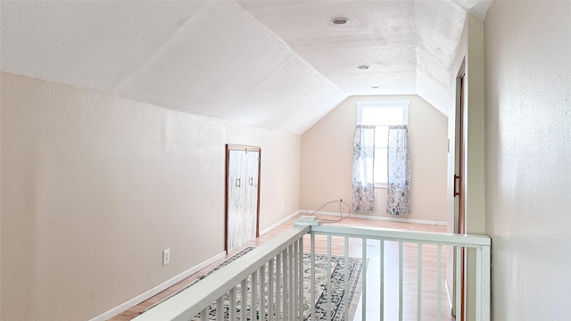 additional living space featuring wood-type flooring, a textured ceiling, and vaulted ceiling