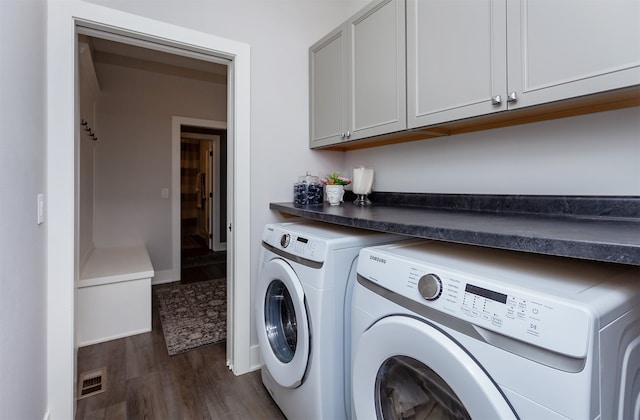 clothes washing area with washing machine and clothes dryer, cabinets, and dark hardwood / wood-style flooring