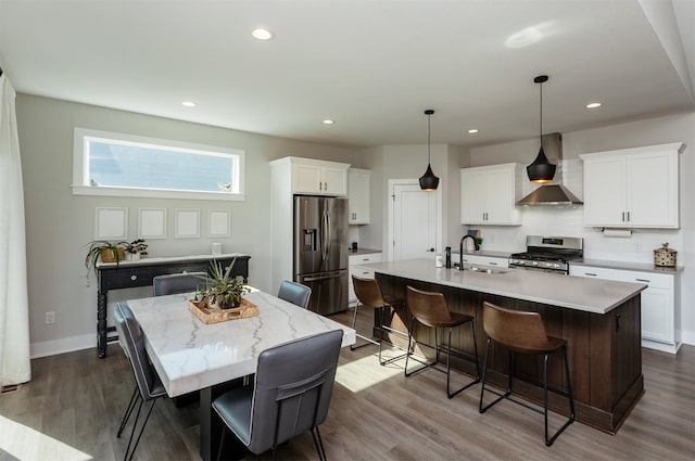 kitchen featuring an island with sink, wall chimney range hood, stainless steel appliances, and white cabinets