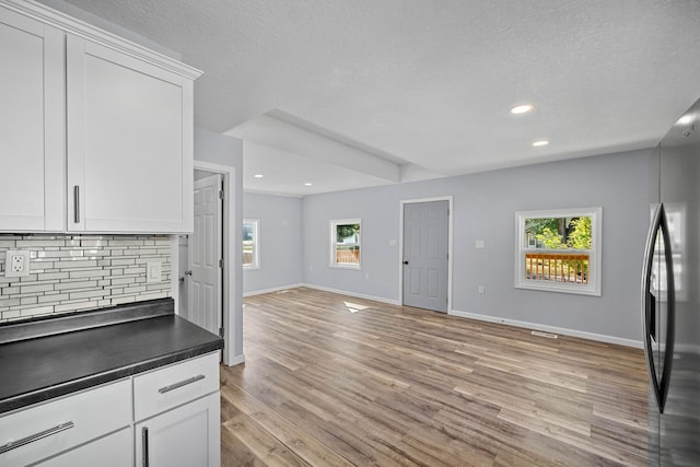 kitchen featuring white cabinets, stainless steel fridge, a textured ceiling, light hardwood / wood-style flooring, and decorative backsplash