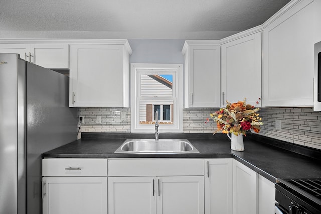 kitchen with backsplash, stainless steel refrigerator, sink, and white cabinets