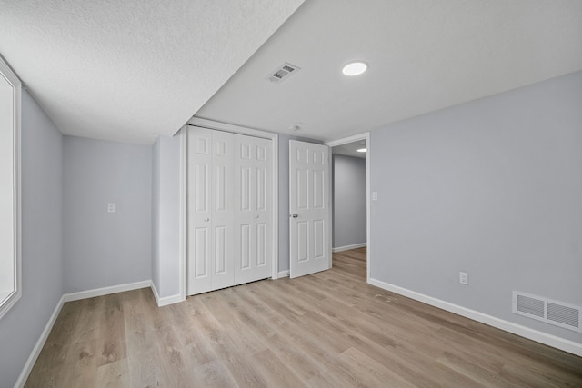 unfurnished bedroom with a textured ceiling, light hardwood / wood-style flooring, and a closet