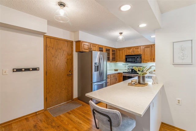 kitchen with kitchen peninsula, appliances with stainless steel finishes, a textured ceiling, light hardwood / wood-style floors, and a breakfast bar area