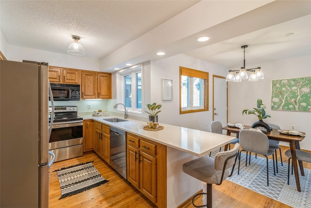 kitchen featuring pendant lighting, sink, light wood-type flooring, a textured ceiling, and appliances with stainless steel finishes