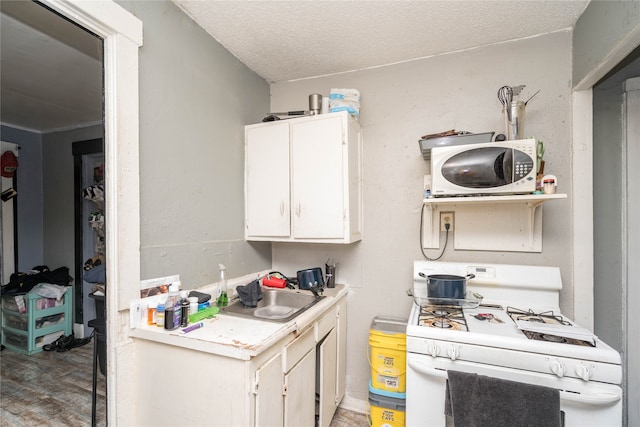 kitchen featuring white appliances, sink, white cabinets, hardwood / wood-style flooring, and a textured ceiling