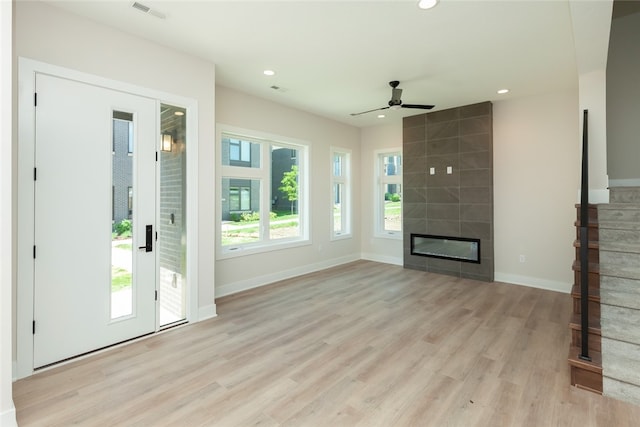 unfurnished living room featuring tile walls, ceiling fan, light hardwood / wood-style flooring, and a tile fireplace