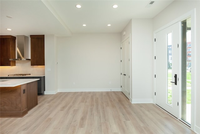 kitchen featuring light wood-type flooring, backsplash, and wall chimney range hood