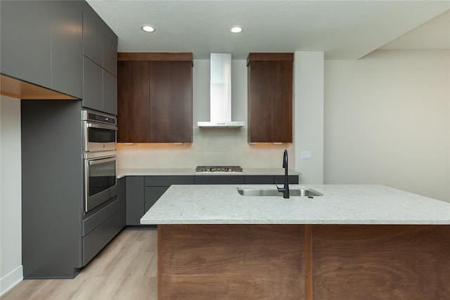 kitchen with light stone countertops, sink, light hardwood / wood-style floors, wall chimney range hood, and appliances with stainless steel finishes