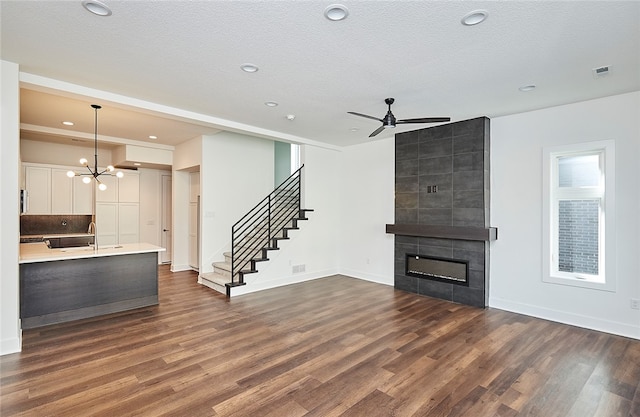 unfurnished living room featuring sink, dark hardwood / wood-style flooring, ceiling fan with notable chandelier, a tile fireplace, and a textured ceiling