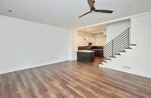 unfurnished living room featuring a textured ceiling, ceiling fan with notable chandelier, and dark hardwood / wood-style flooring