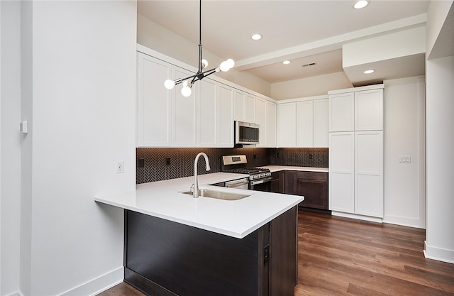 kitchen featuring sink, dark hardwood / wood-style flooring, kitchen peninsula, appliances with stainless steel finishes, and decorative light fixtures