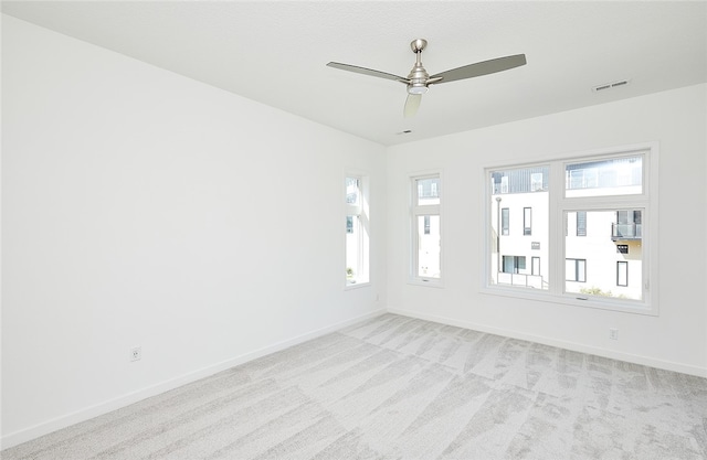 spare room featuring light carpet, ceiling fan, and a wealth of natural light