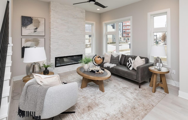 living room featuring ceiling fan, a stone fireplace, and light hardwood / wood-style flooring