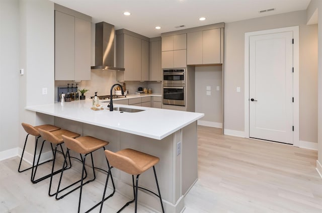 kitchen with a kitchen breakfast bar, kitchen peninsula, gray cabinetry, and wall chimney exhaust hood