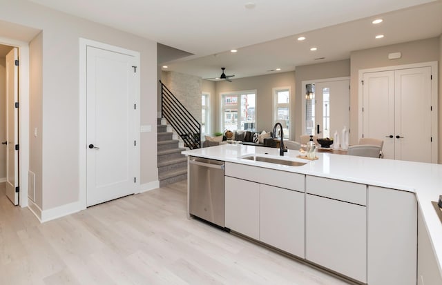 kitchen with stainless steel dishwasher, ceiling fan, sink, light wood-type flooring, and white cabinets