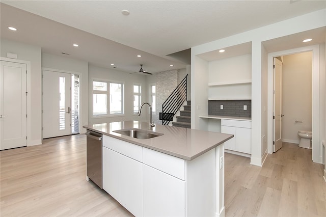 kitchen featuring stainless steel dishwasher, sink, white cabinetry, light hardwood / wood-style flooring, and a center island with sink