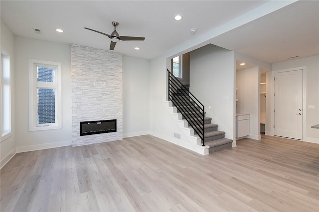 unfurnished living room featuring ceiling fan, light wood-type flooring, and a stone fireplace