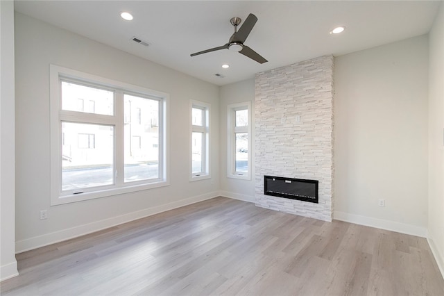 unfurnished living room with ceiling fan, light hardwood / wood-style flooring, and a stone fireplace