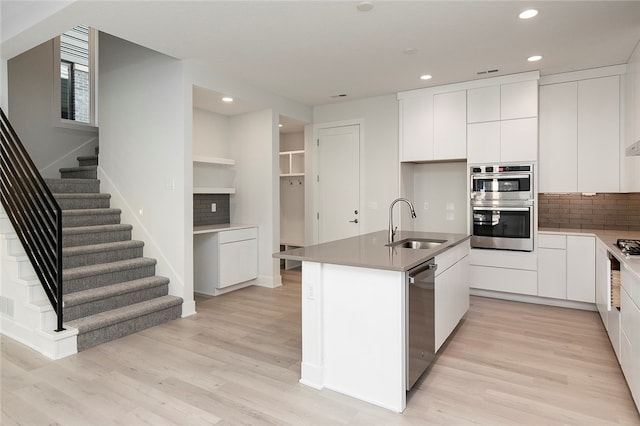 kitchen featuring decorative backsplash, a kitchen island with sink, white cabinets, sink, and appliances with stainless steel finishes