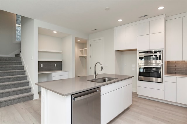 kitchen featuring light wood-type flooring, sink, stainless steel appliances, an island with sink, and white cabinets