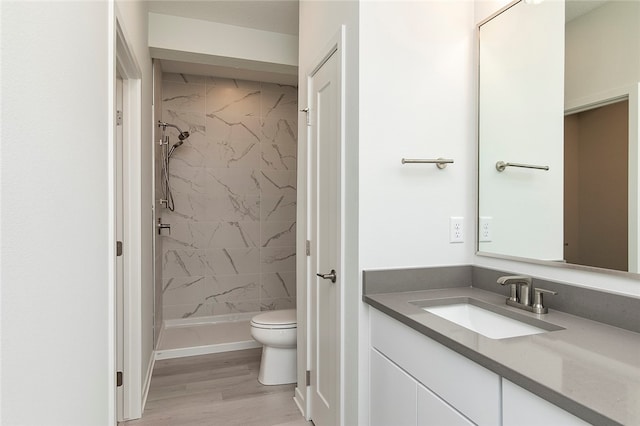 bathroom featuring a tile shower, vanity, toilet, and wood-type flooring