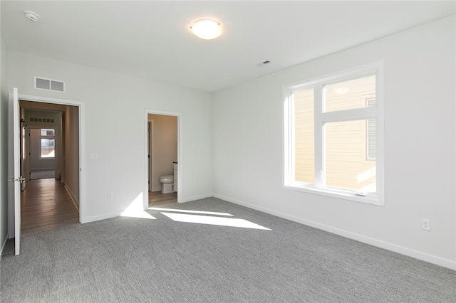 unfurnished bedroom featuring carpet floors, ensuite bath, and multiple windows