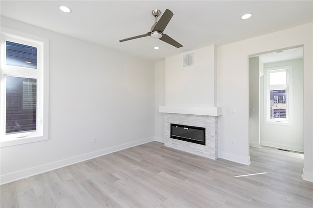 unfurnished living room with ceiling fan, a stone fireplace, and light hardwood / wood-style flooring