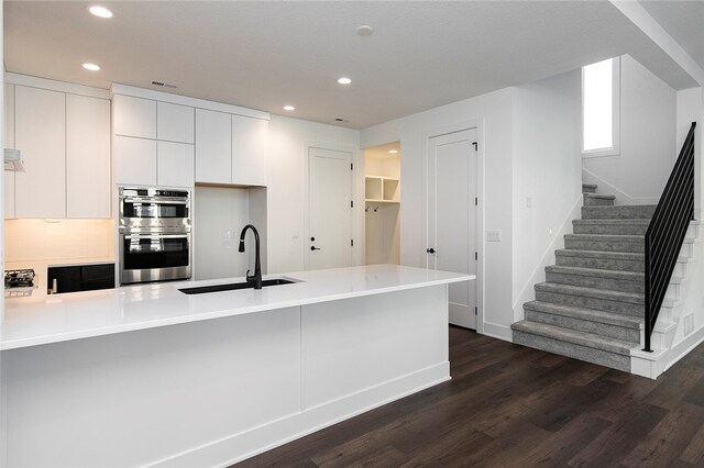 kitchen featuring sink, kitchen peninsula, white cabinetry, double oven, and dark hardwood / wood-style floors