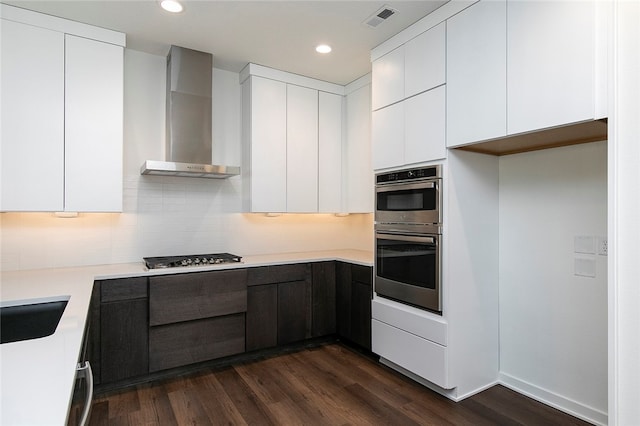 kitchen featuring wall chimney exhaust hood, appliances with stainless steel finishes, dark hardwood / wood-style flooring, and white cabinetry