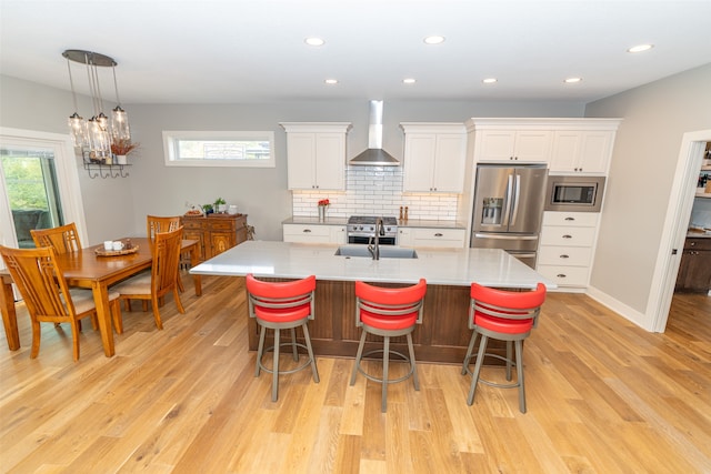 kitchen featuring appliances with stainless steel finishes, wall chimney exhaust hood, white cabinetry, and a healthy amount of sunlight