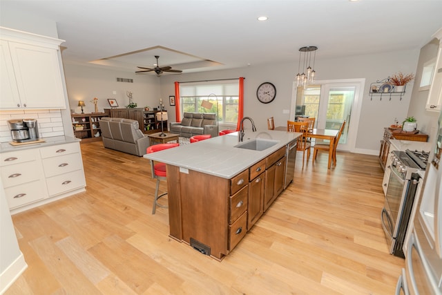 kitchen featuring white cabinets, a kitchen island with sink, decorative light fixtures, appliances with stainless steel finishes, and light hardwood / wood-style floors