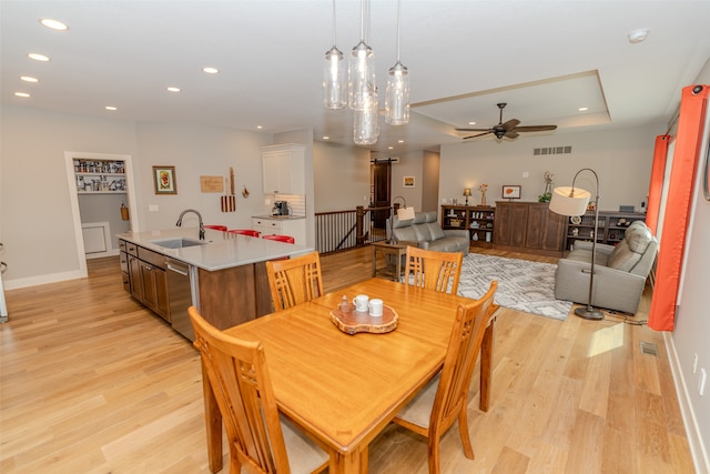 dining area with light hardwood / wood-style flooring, ceiling fan with notable chandelier, and sink