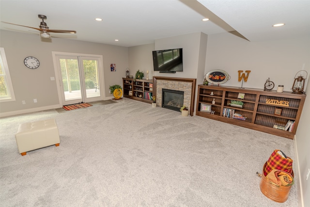 living room featuring ceiling fan, a stone fireplace, and carpet flooring