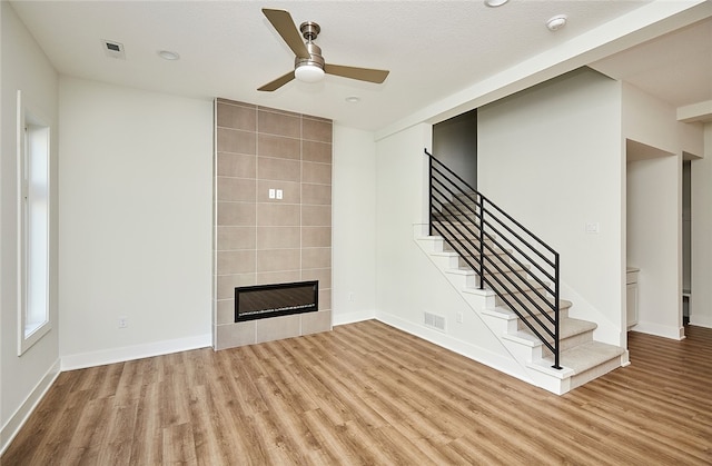 unfurnished living room featuring ceiling fan, a textured ceiling, light hardwood / wood-style flooring, a tile fireplace, and tile walls