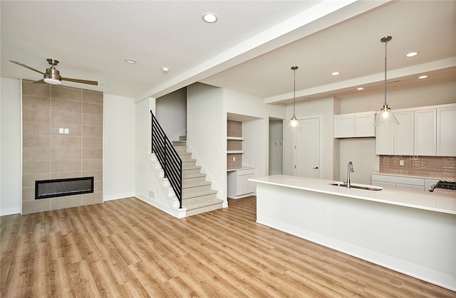 kitchen with light wood-type flooring, sink, a fireplace, hanging light fixtures, and white cabinetry